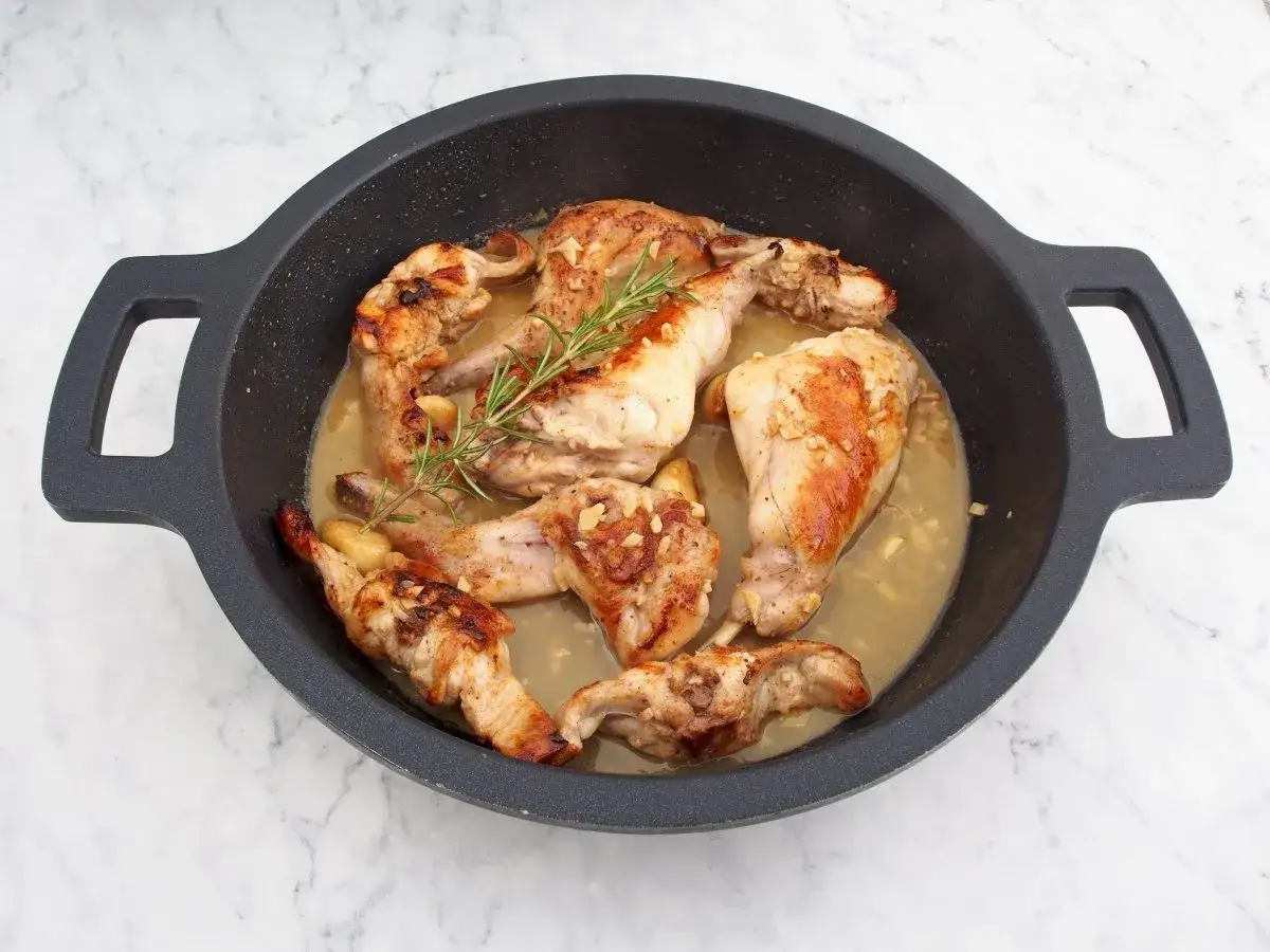 Sabroso conejo al ajillo en una sartén, con trozos dorados de carne, ajo picado y una ramita de romero fresco.