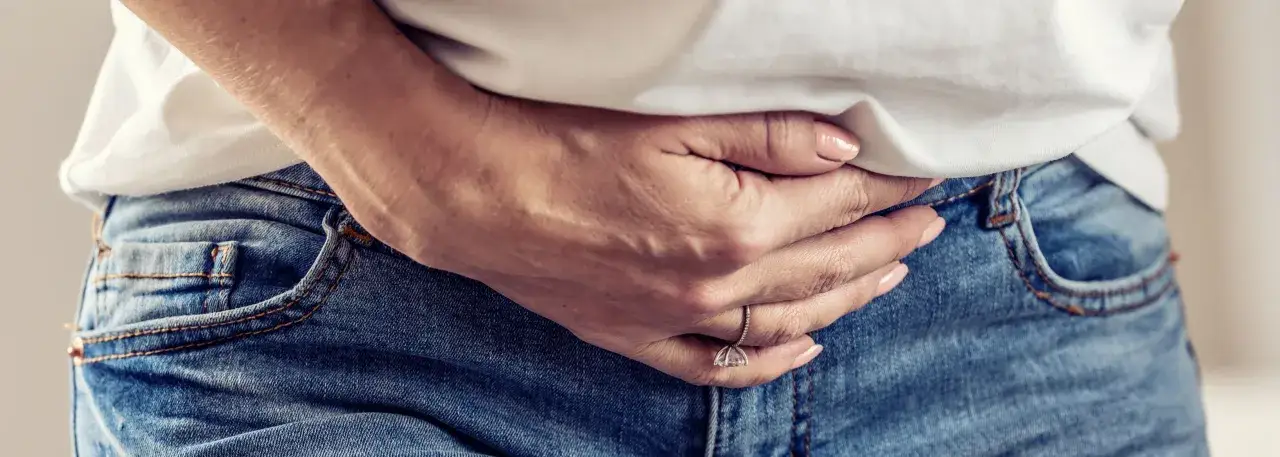 Dłoń obejmuje brzuch, sugerując ból brzucha, który może być objawem zatrucia jadem kiełbasianym u dorosłych.