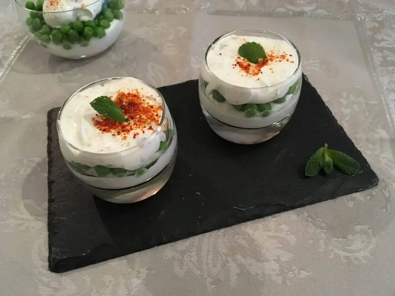 Deux verrines de mousse de chèvre et petits pois, garnies de menthe et de paprika.