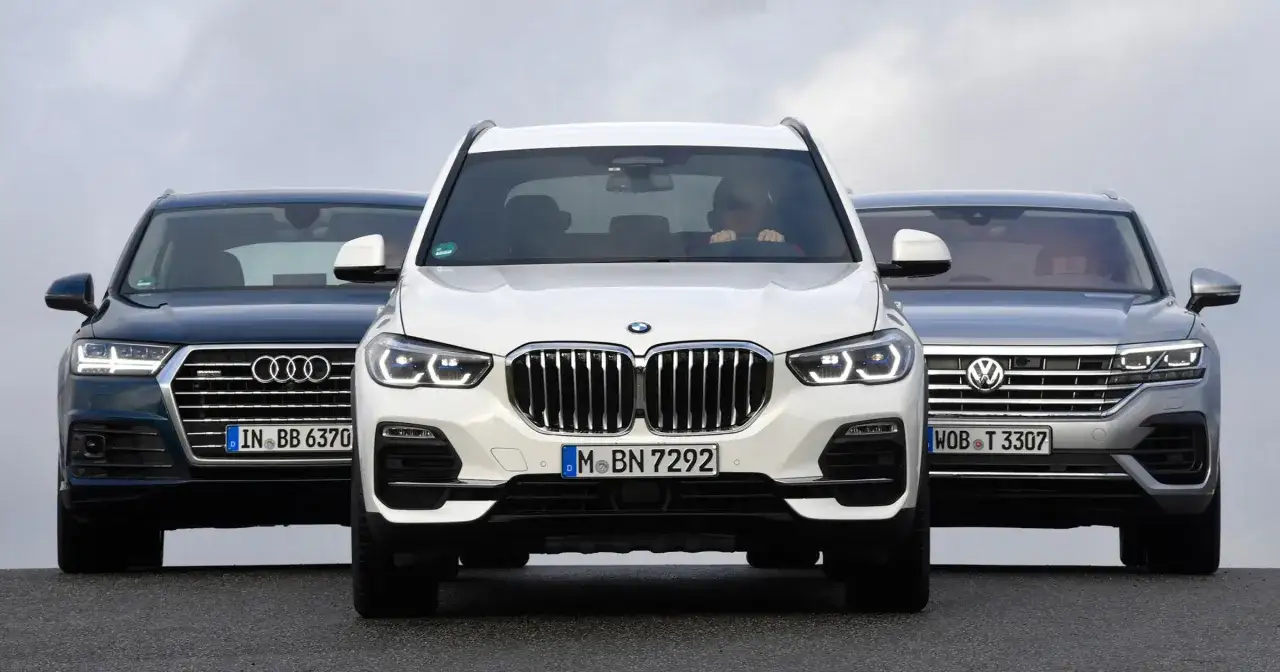 Trzy SUV-y: białe BMW X9, ciemny Audi Q7 i srebrny Volkswagen Touareg stoją obok siebie.