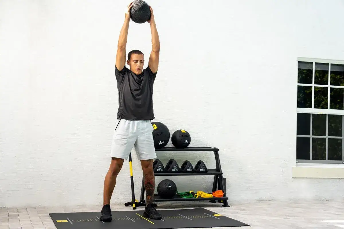 Uomo esegue esercizi efficaci addominali con un peso sopra la testa. Attrezzatura da palestra sullo sfondo.