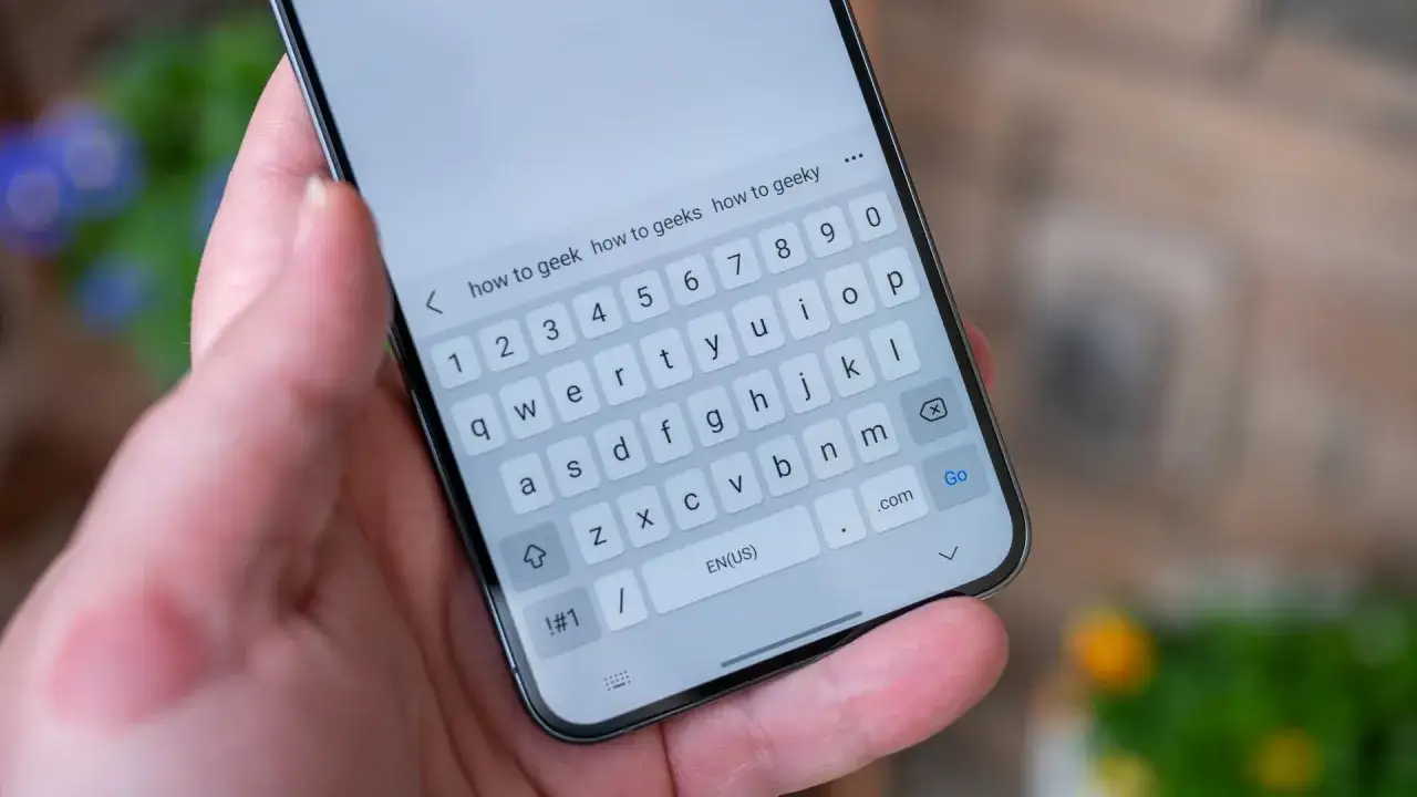 Dłoń trzyma smartfon z klawiaturą ekranową. Szukam informacji, gdzie jest schowek w telefonie, wpisując 
