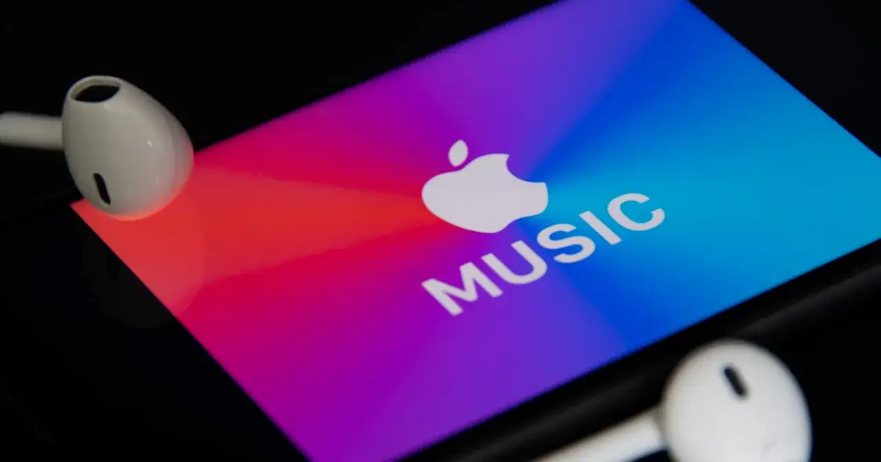 Słuchawki AirPods leżą obok ekranu telefonu z logo Apple Music. Sprawdź aktualną apple music cena.