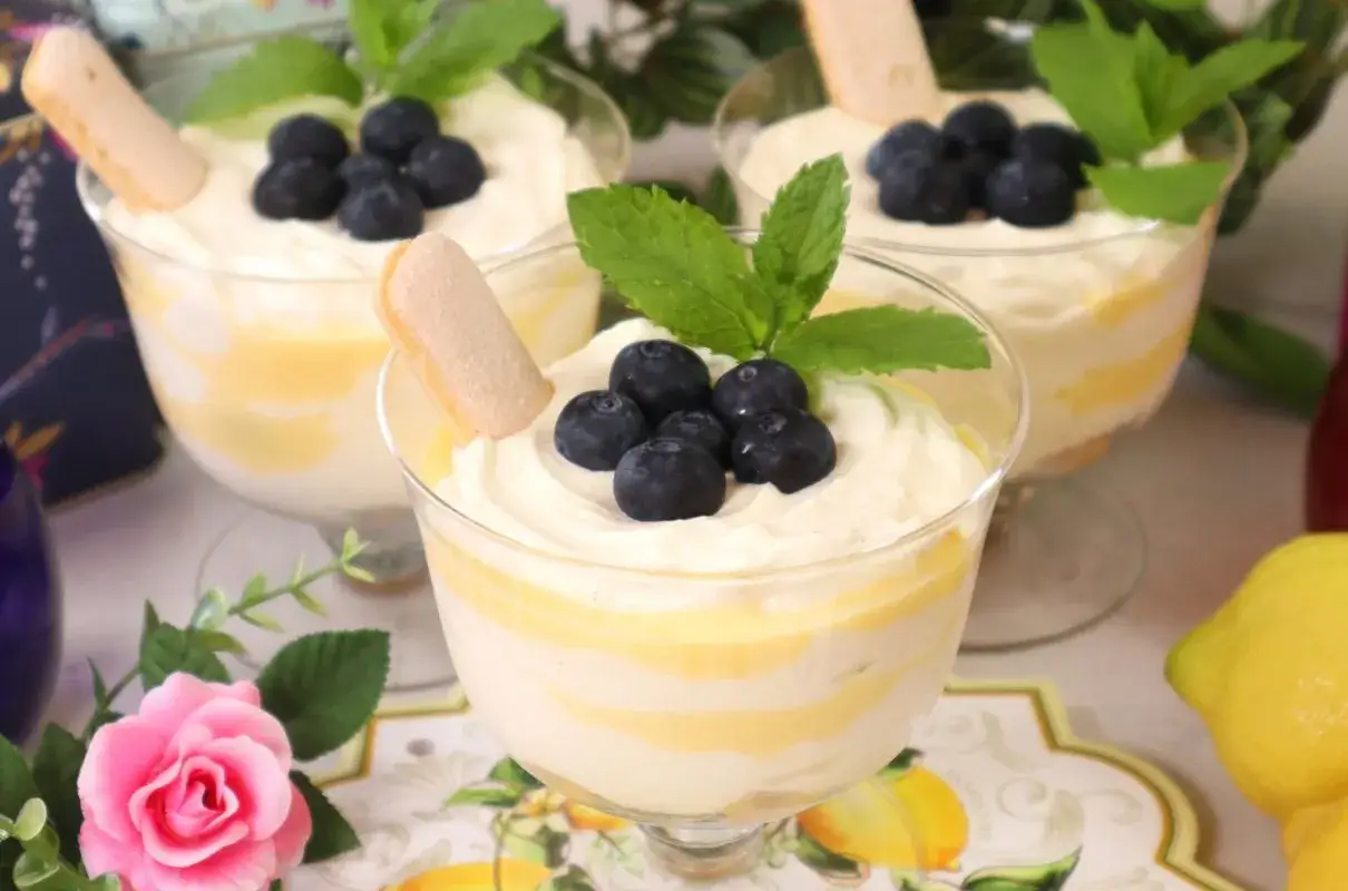 Pyszny deser z warstwami kremu i cytrynowego curd, ozdobiony jagodami i biszkoptem. Idealny przepis na lemon curd!