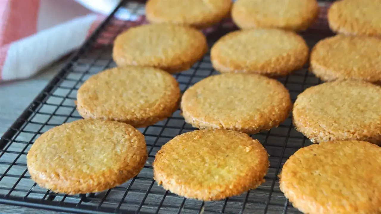 Galletas de coco doradas y crujientes enfri&aacute;ndose en una rejilla.