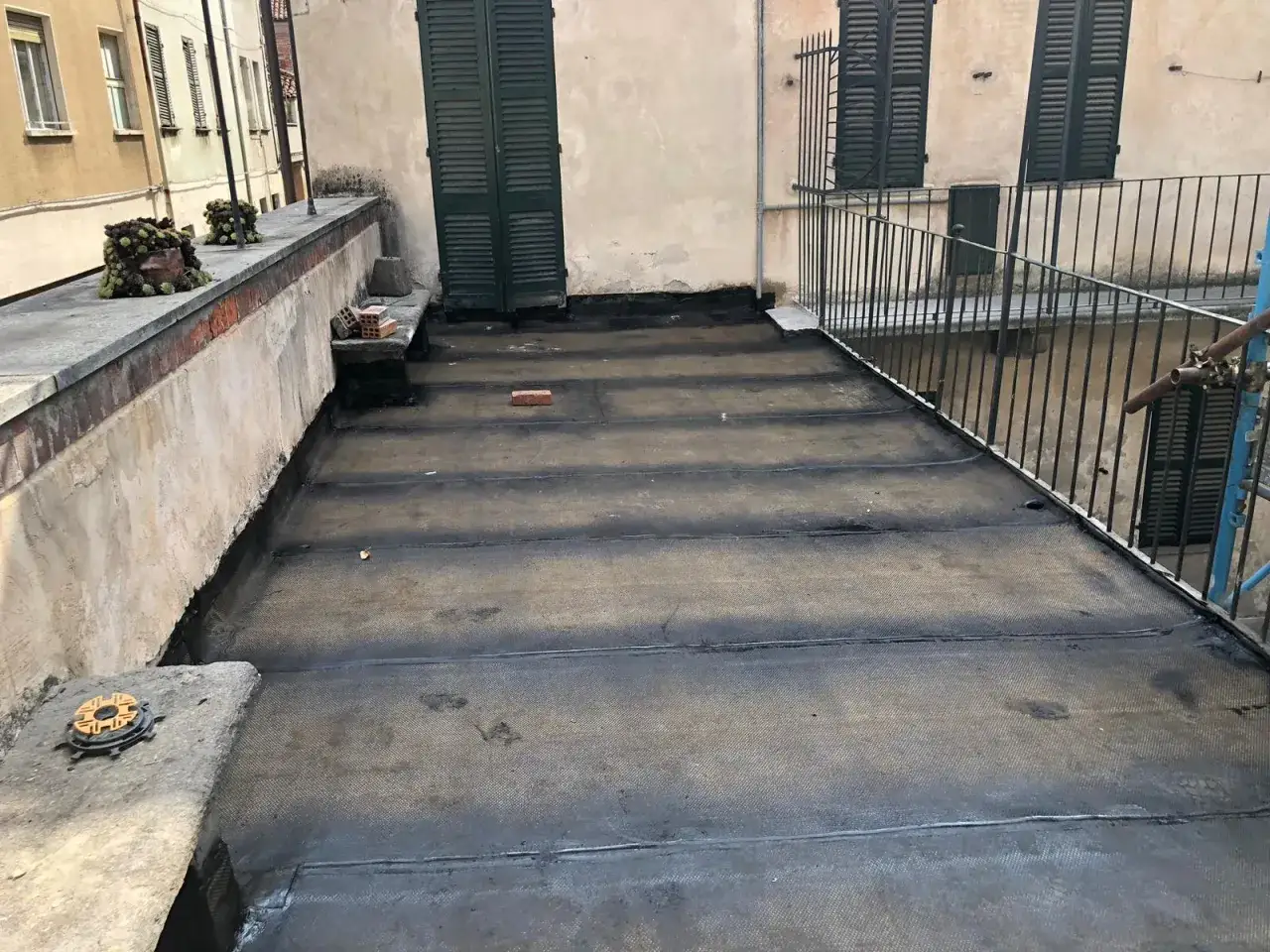Un terrazzo sul tetto con guaina bituminosa appena posata. Mattoni e vasi con piante decorano il bordo.