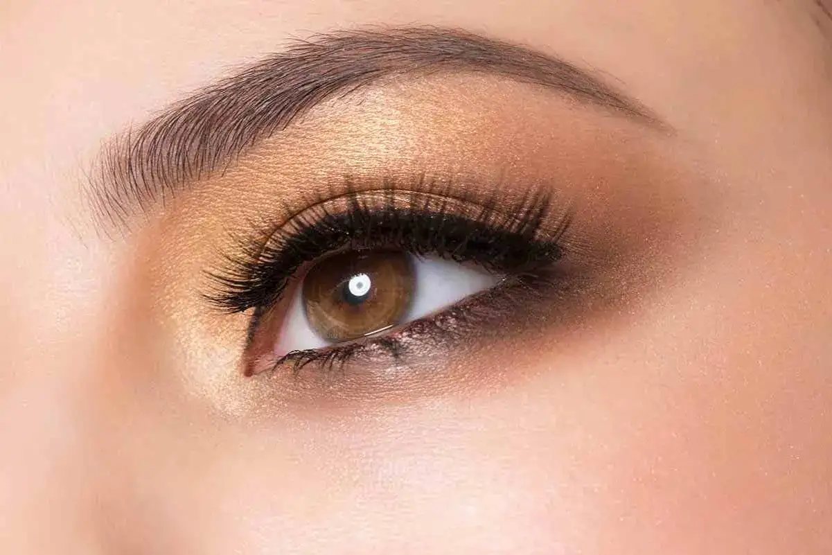 Ojos marrones realzados con un maquillaje dorado y ahumado, pesta&ntilde;as largas y cejas definidas.