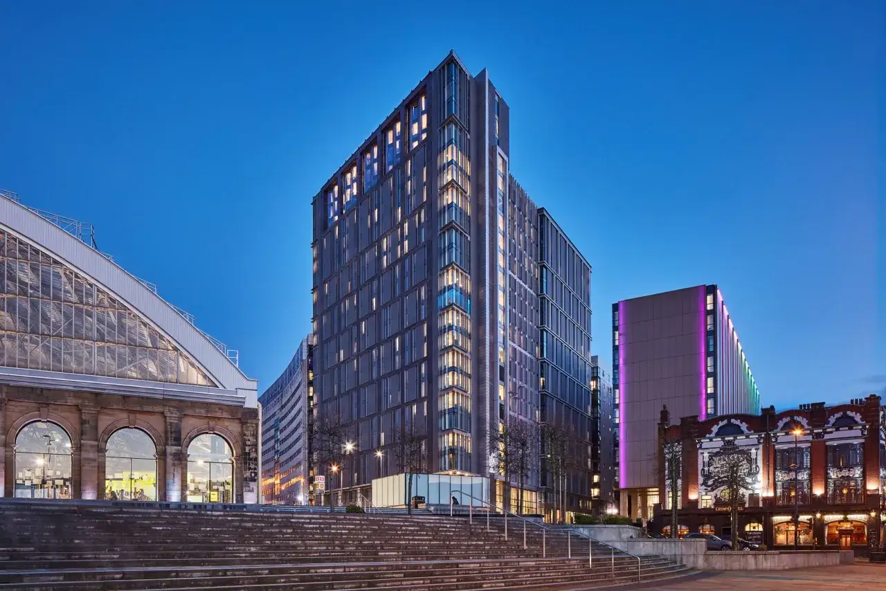 Edificios modernos y una estructura de cristal iluminados al anochecer en Liverpool. Horizon Heights se alza majestuoso, con luces cálidas brillando desde sus ventanas.