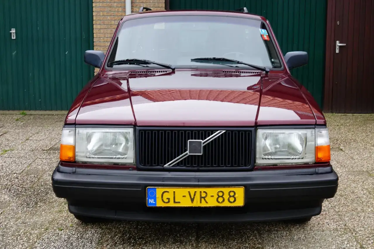 En mörkröd Volvo Polar står parkerad framför en grön garageport.