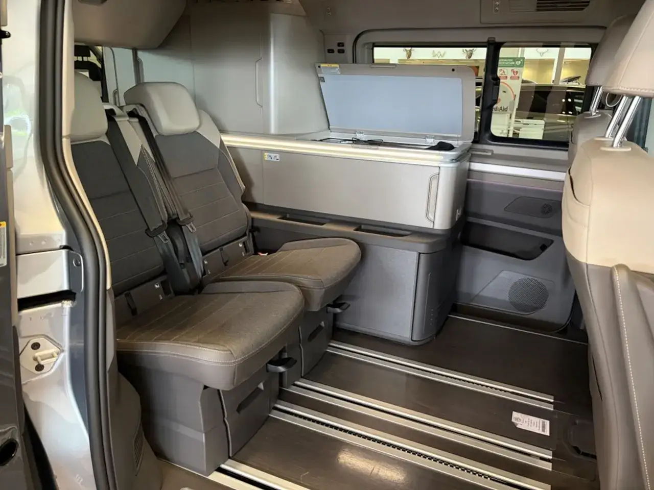 Interiör i en Volkswagen plåtis med två säten framåt, ett kök med öppen lucka och ett kylskåp. Perfekt för äventyr!