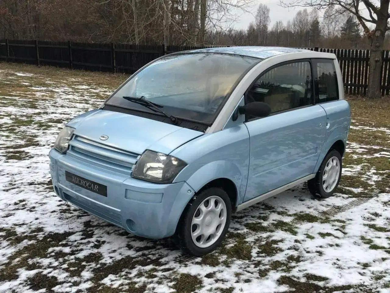 Niebieski Microcar, idealny jako auto bez prawa jazdy, stoi na zaśnieżonej trawie.