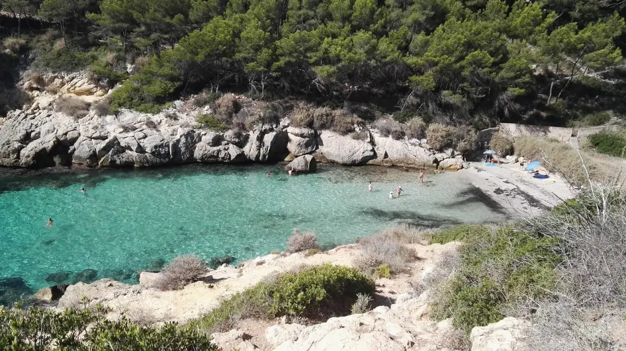 Es cal&oacute; de la bella dona, una cala escondida con aguas turquesas y rocas escarpadas, donde algunas personas disfrutan del sol y el mar.