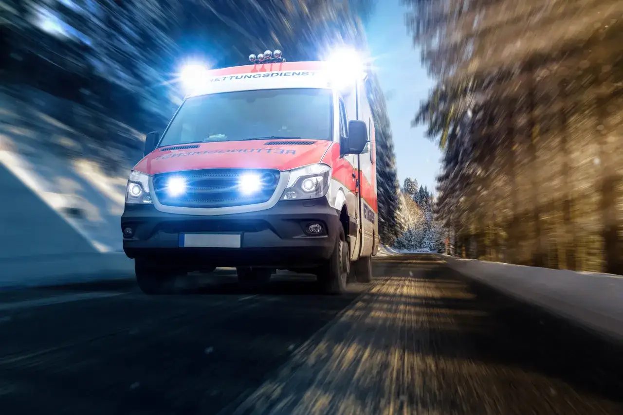 Ambulans z włączonymi sygnałami świetlnymi pędzi zimową drogą przez las. Te pojazdy uprzywilejowane zawsze spieszą z pomocą.