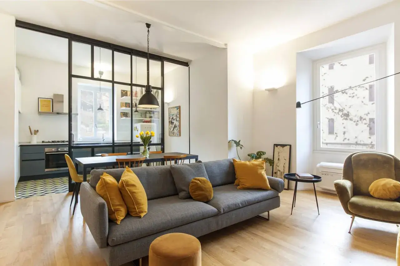 Soggiorno moderno con divano grigio, poltrona verde e cucina a vista separata da vetrata. Ottime idee living open space.