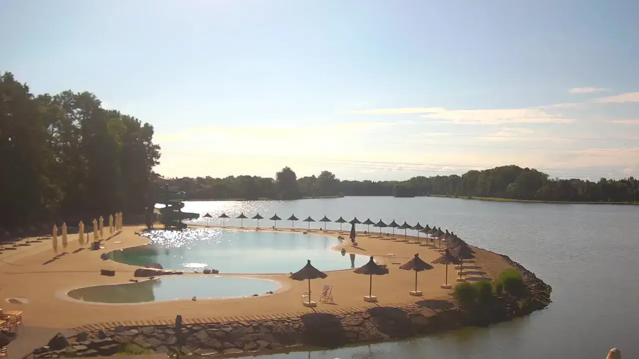 Słoneczny dzień nad zalewem Osiek. Piaszczysta plaża z parasolami i leżakami, woda lśni w słońcu.