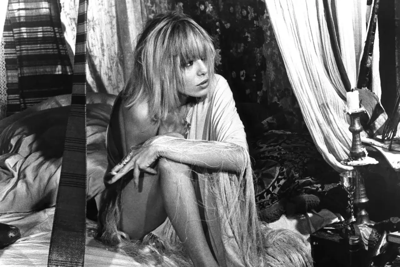 Anita Pallenberg, icona di stile e musa rock, posa in un letto dall'atmosfera boh&eacute;mien, circondata da tessuti e candele.