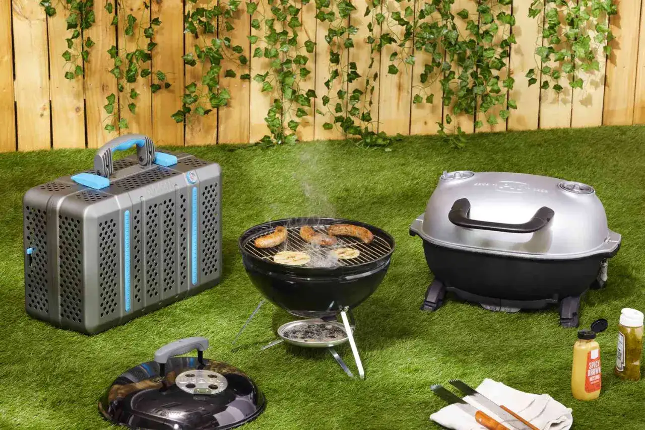 En b&auml;rbar kolgrill med korv och br&ouml;d p&aring; grillen. Bredvid st&aring;r en annan grill och en grillv&auml;ska.