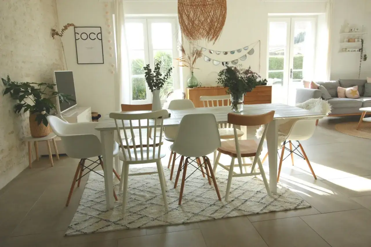 Salle à manger lumineuse avec table en bois clair et chaises dépareillées, créant une ambiance tendance et chaleureuse.