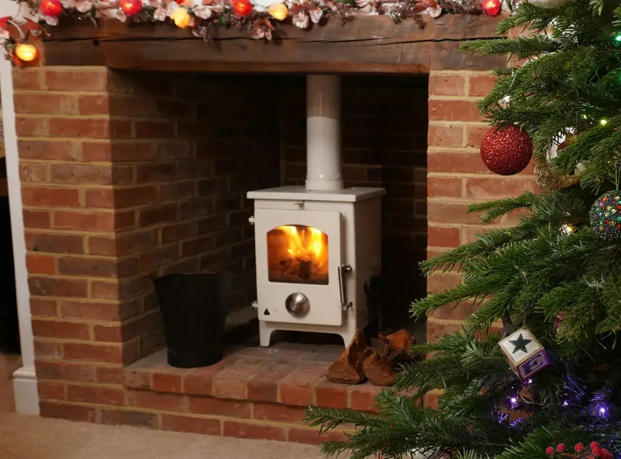 Un poêle à pellets blanc est installé dans une cheminée en briques, prêt pour un raccordement. Un sapin de Noël décoré est à droite.