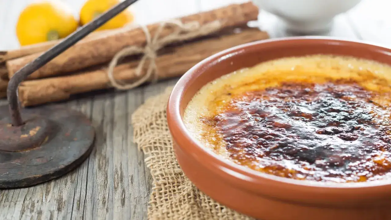 Crema catalana receta: postre con capa caramelizada crujiente, canela y limones de fondo.