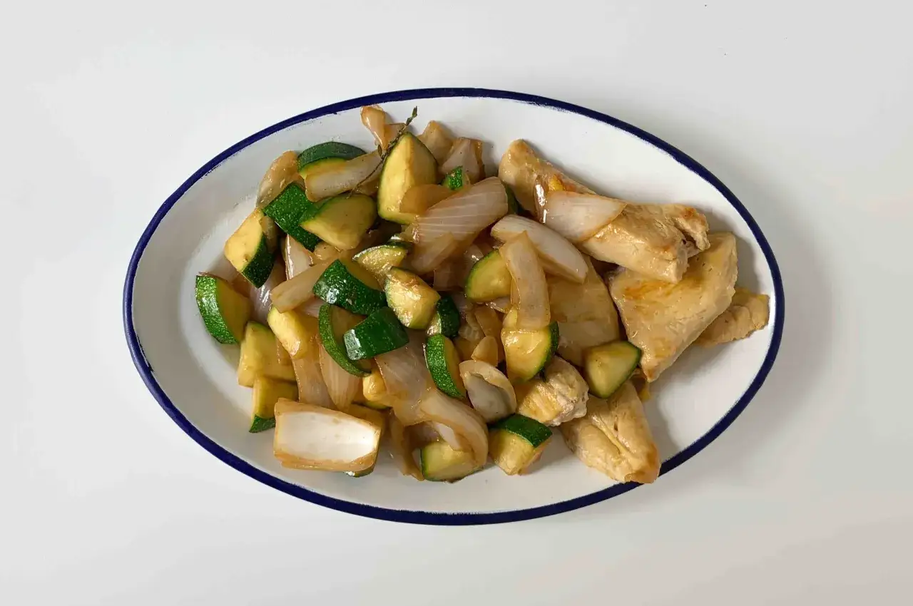 Sabroso pollo con calabac&iacute;n y cebolla salteados en un plato blanco con borde azul.