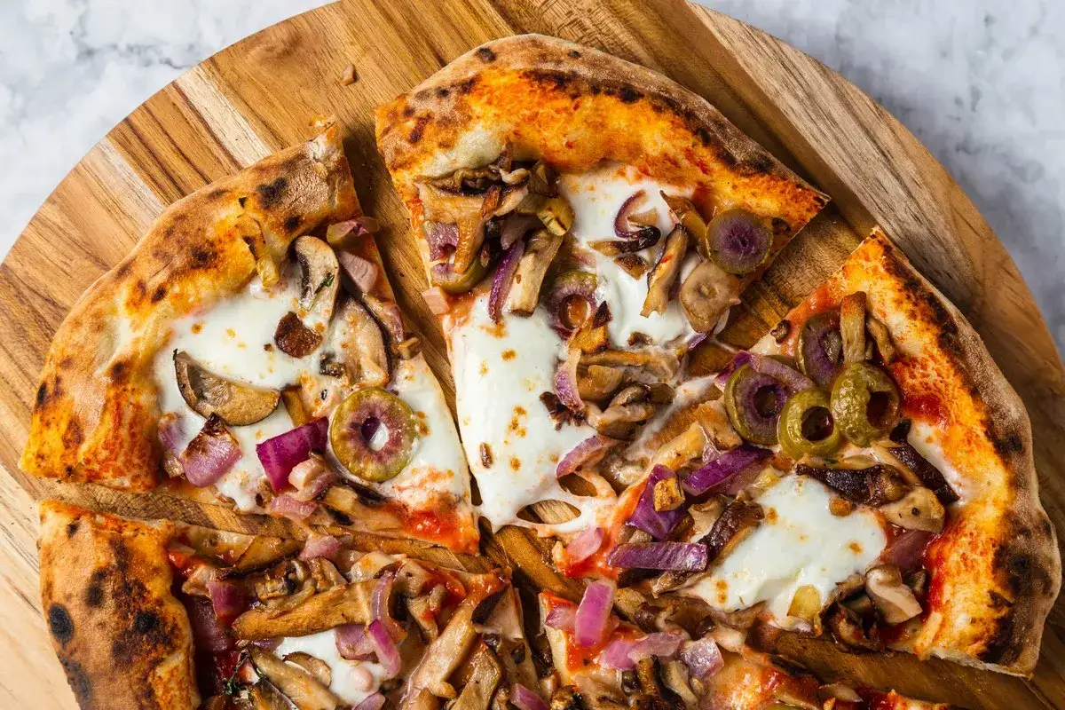 Pizza z pieczarkami, oliwkami i czerwoną cebulą, posypana serem. Surowe pieczarki na pizzy dodają jej wyjątkowego smaku.