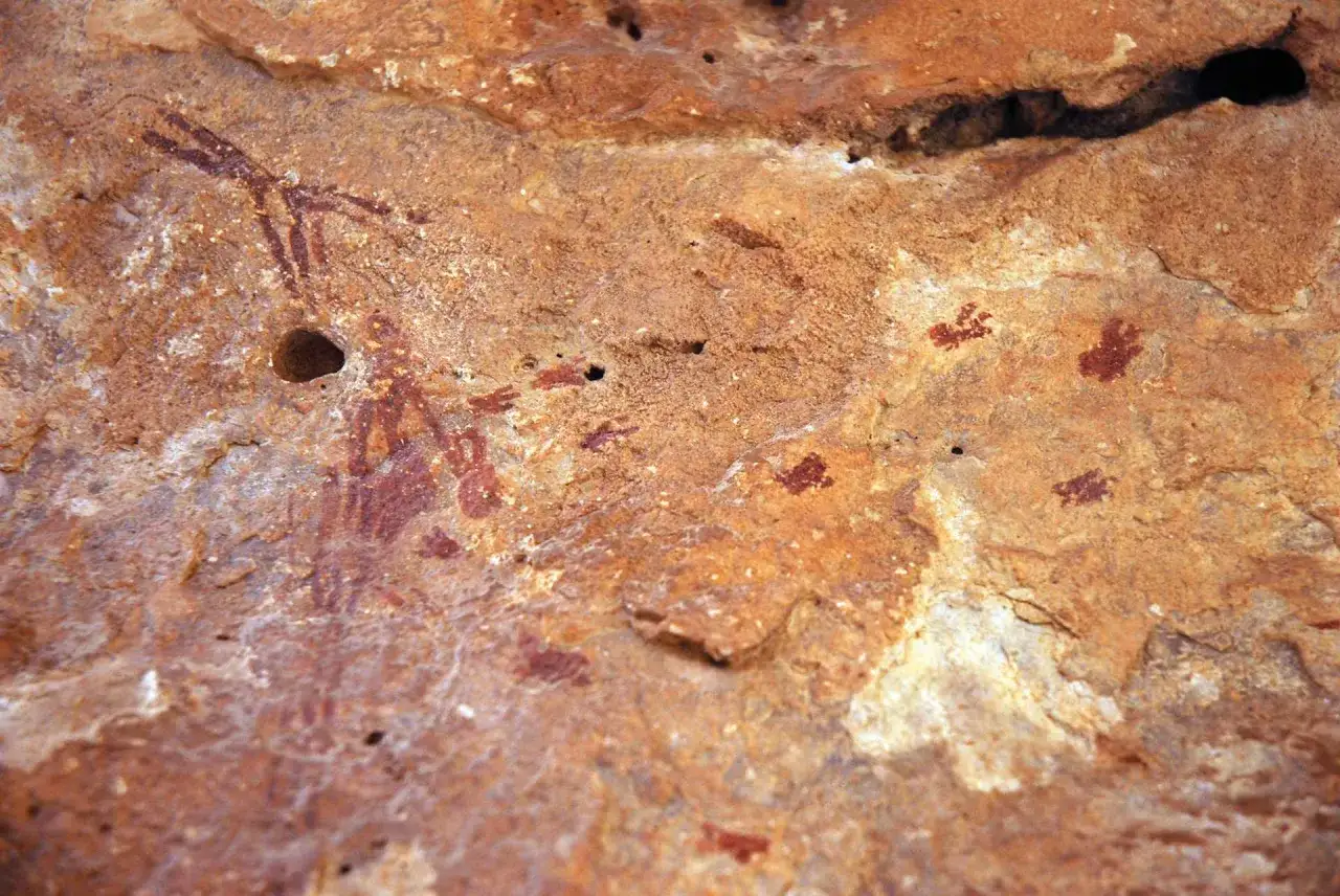 Pinturas rupestres en la cueva de la araña: figuras antropomorfas y huellas de manos rojas sobre roca ocre.