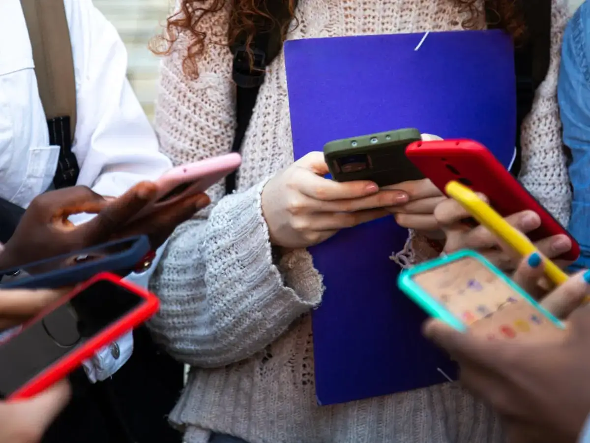 Grupa młodych ludzi skupiona na telefonach, każdy pogrążony w swoim cyfrowym świecie. Czy to już uzależnienie od telefonu?
