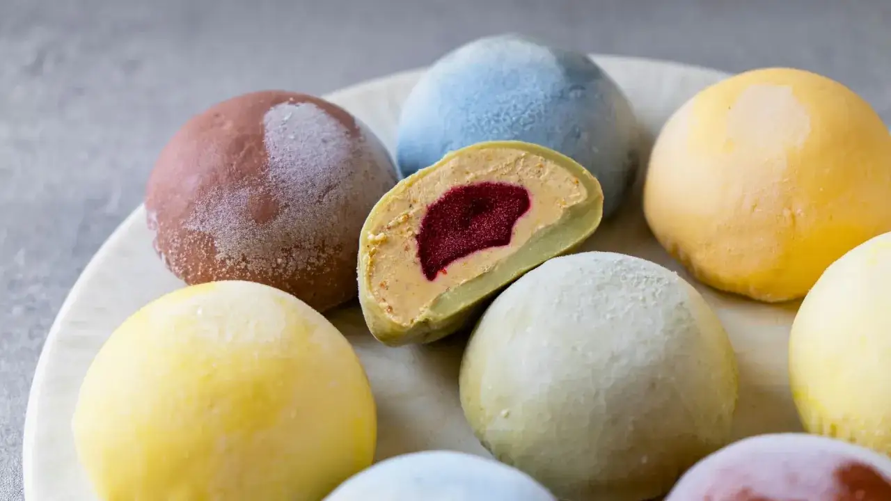 Kolorowe mochi, w tym jedno przekrojone, ukazujące kremowe nadzienie z owocowym środkiem. Pytasz mochi co to? To pyszny deser!