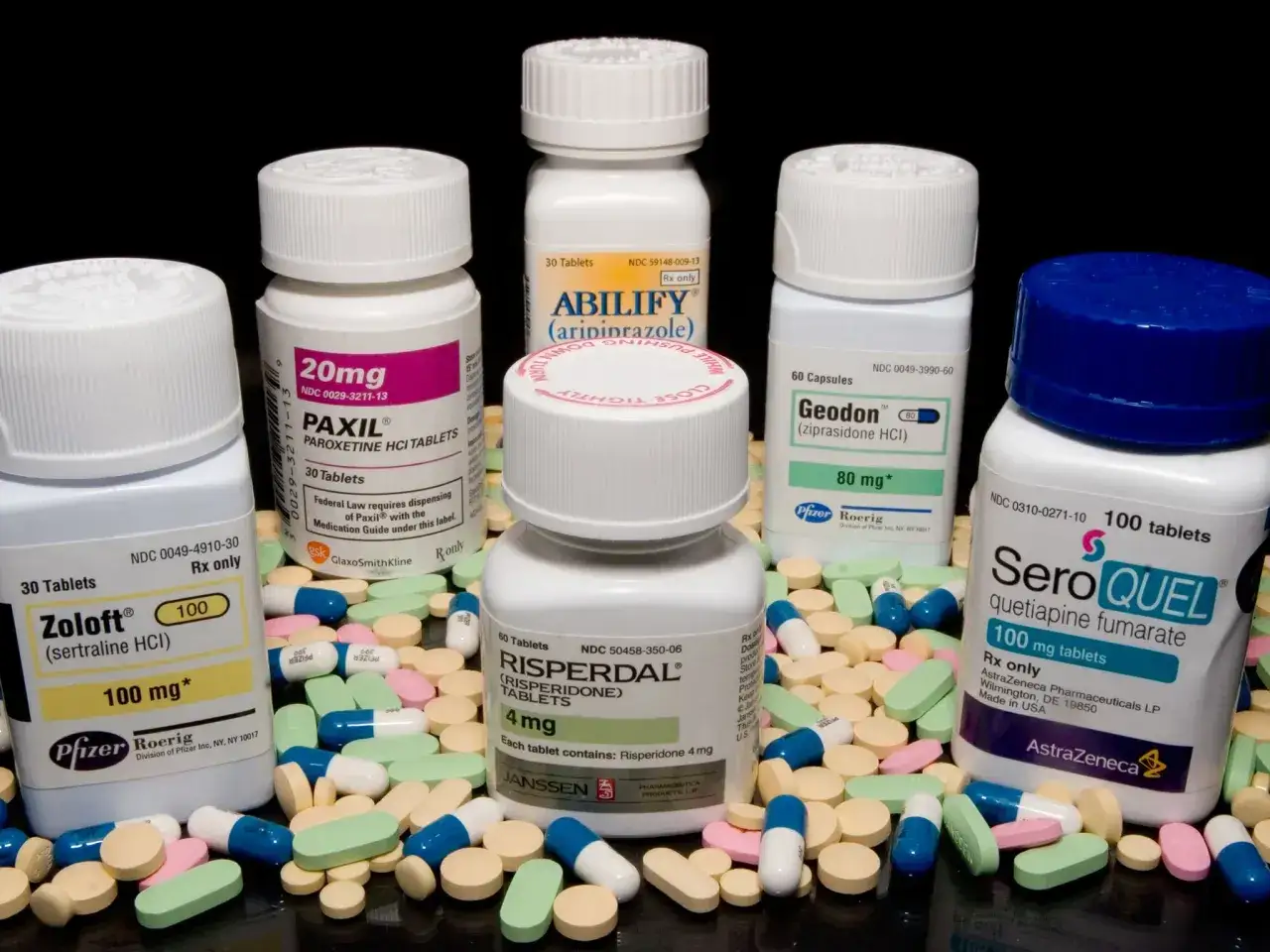 Leki na receptę, w tym Seroquel (kwetiapina), Paxil, Zoloft, Abilify, Geodon i Risperdal, leżą wśród kolorowych tabletek.