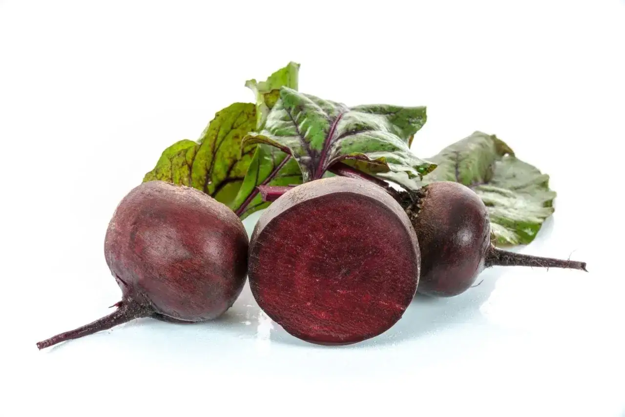Drei frische rote Bete, eine davon angeschnitten, mit grünen Blättern auf weißem Hintergrund.