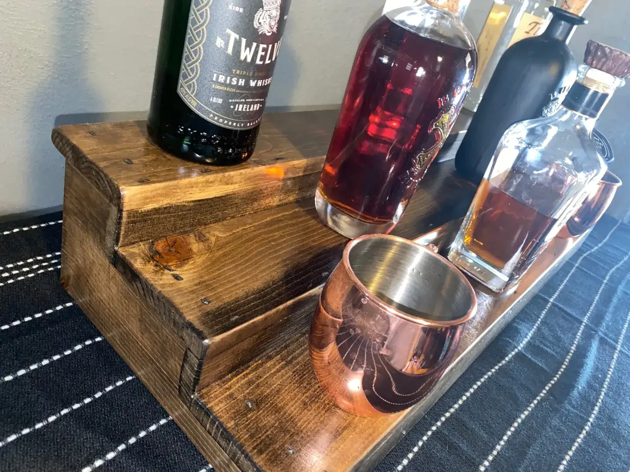 Flaschen mit Whiskey auf Holzdisplay. Die Frage, ob kann Whiskey schlecht werden, beschäftigt Genießer. Hier sind einige Flaschen und ein Kupferbecher.