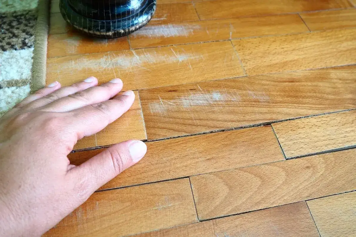 Mano che controlla il parquet graffiato, pronto per levigare marmo con carta vetrata per un restauro.