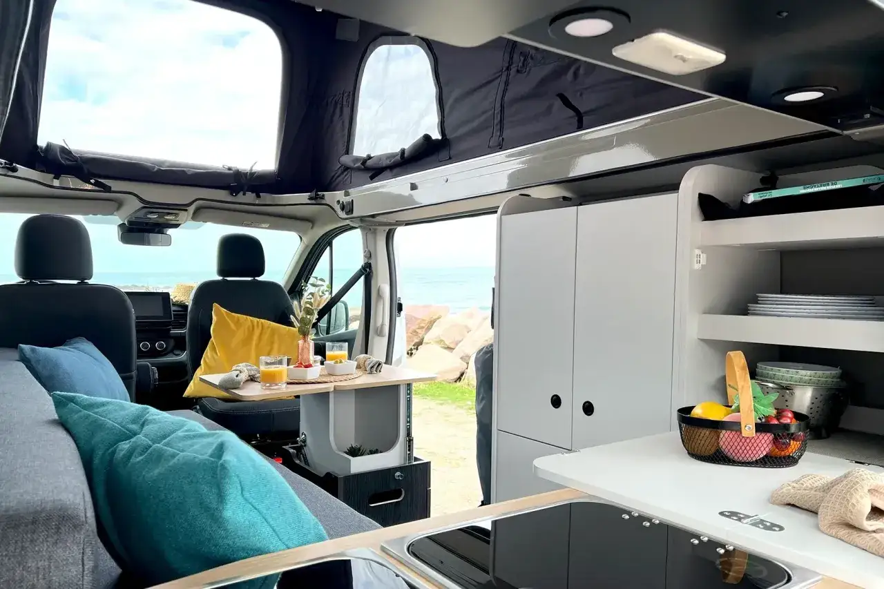 Aménagement d'un van pour 4 : salon cosy, table pour le petit-déjeuner face à la mer, cuisine fonctionnelle et couchages confortables.