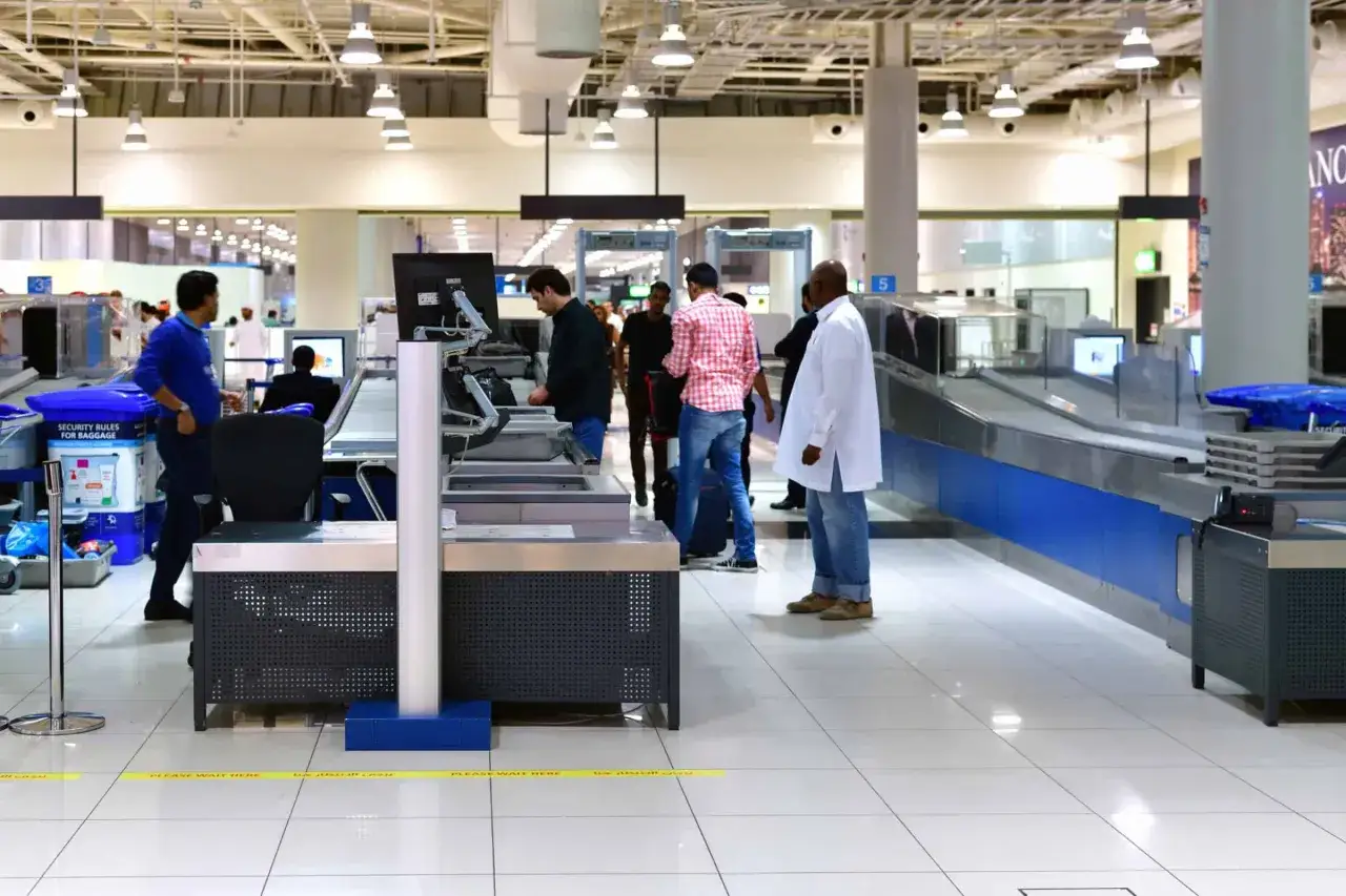 Menschen stehen an Gepäckbändern und Sicherheitskontrollen im Dubai Airport Transit.