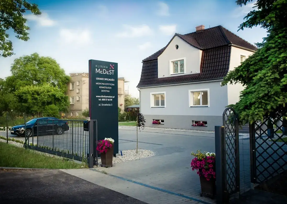 Klinika Medest w Opolu z tablicą informacyjną, budynkiem i samochodem.