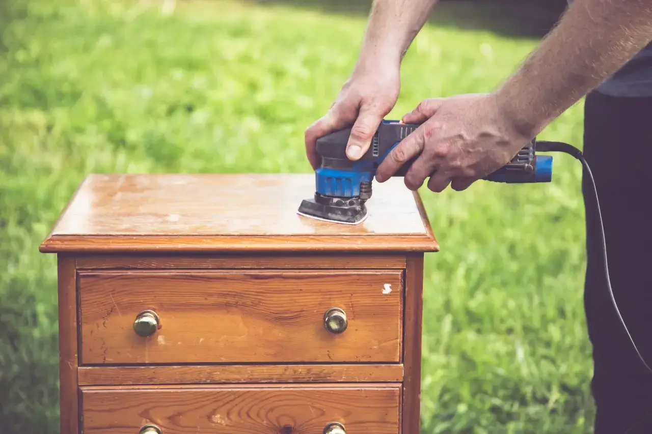 Homme ponçant un meuble en bois pour comment décaper un meuble en bois foncé. L'outil électrique enlève la vieille finition.