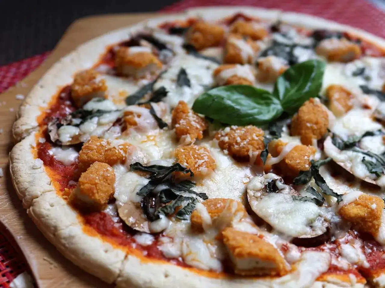 Pizza mit knusprigen Hähnchen-Nuggets, Pilzen, Basilikum und geschmolzenem Käse, bestreut mit feinem parmesan.