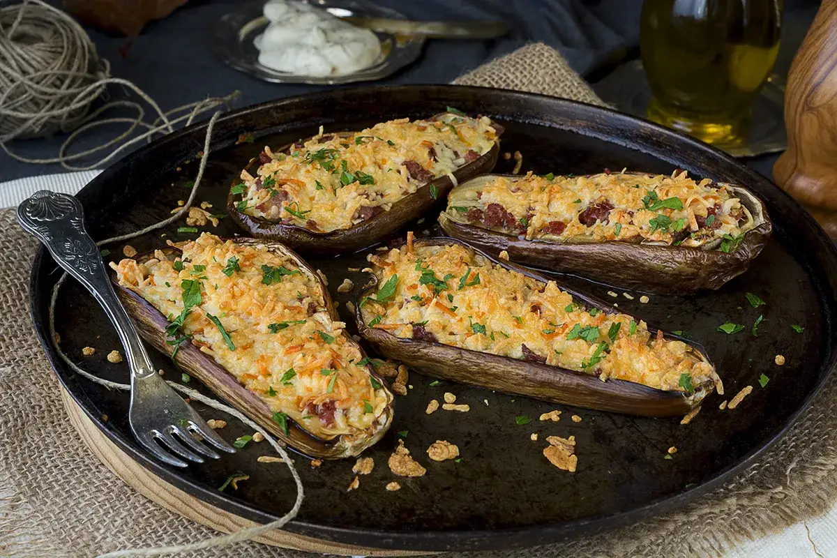 Cuatro mitades de berenjenas rellenas, gratinadas con queso y perejil, listas para disfrutar como berenjenas a la parmesana.