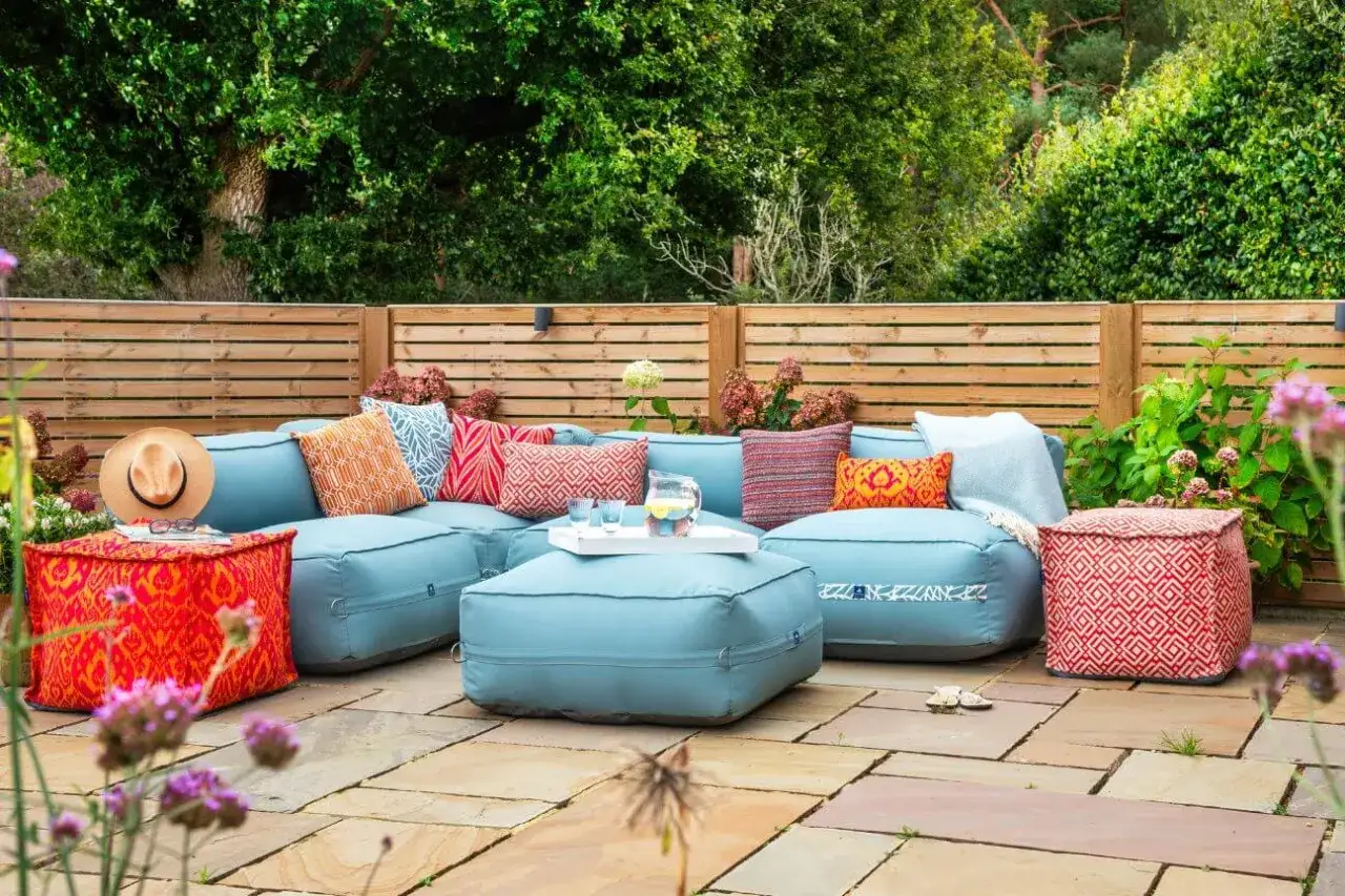 Gem&uuml;tliche Gartenlounge mit hellblauen Polstern und bunten Kissen. Ein kleiner Regenschauer hat die gartenpolster nass geworden, aber die Farben leuchten trotzdem.