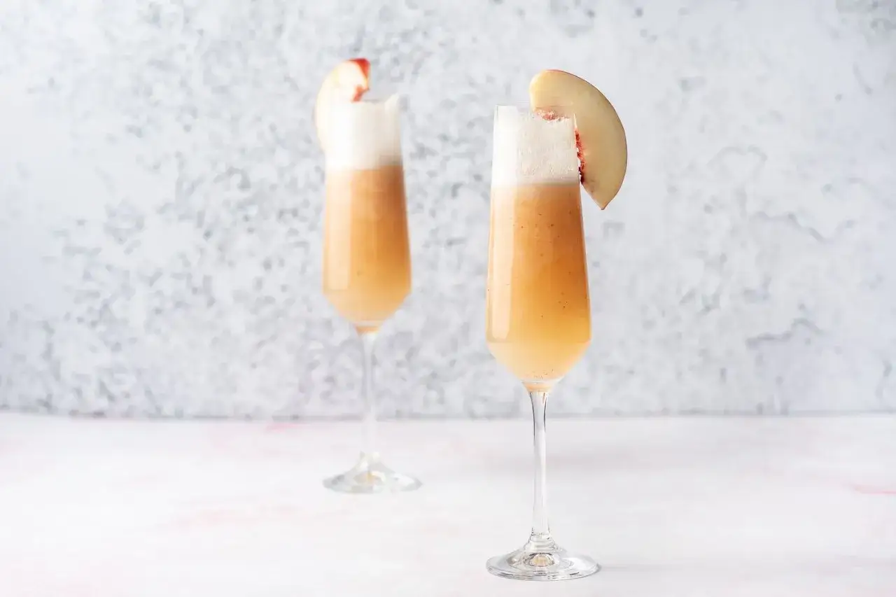 Tv&aring; glas med en bubblig bellini drink, garnerade med persikoklyftor.