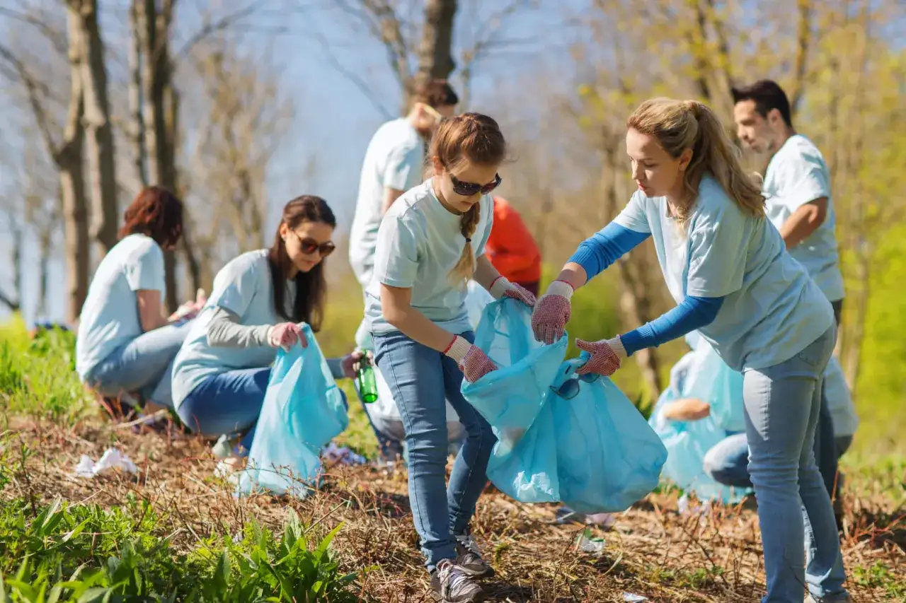 Volunteers participate in a charity event, cleaning up a park by collecting litter in blue bags.