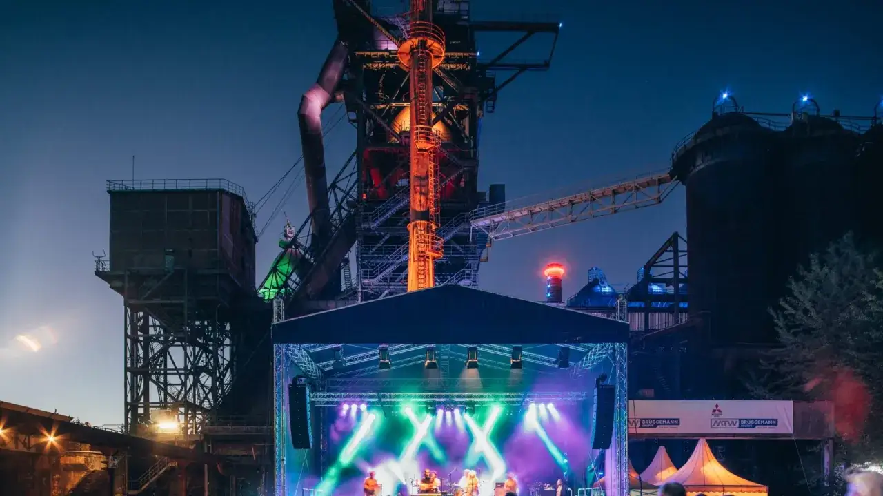 B&uuml;hne mit Band vor Industriekulisse bei Festivals NRW. Bunte Lichter beleuchten die Nacht.