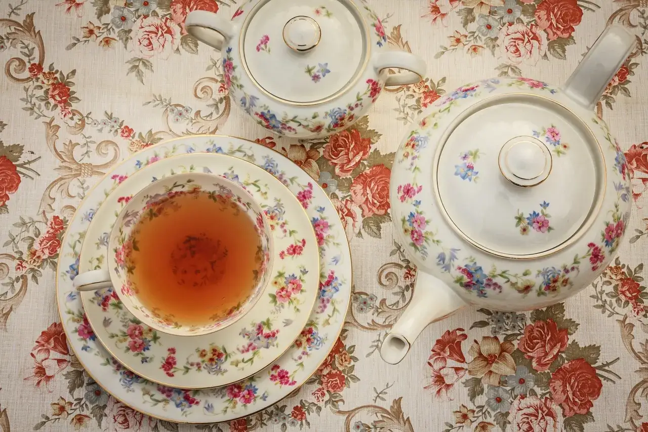 Service à thé fleuri, une tasse remplie de thé ambré, une théière et un sucrier. Une belle tradition de tea time.