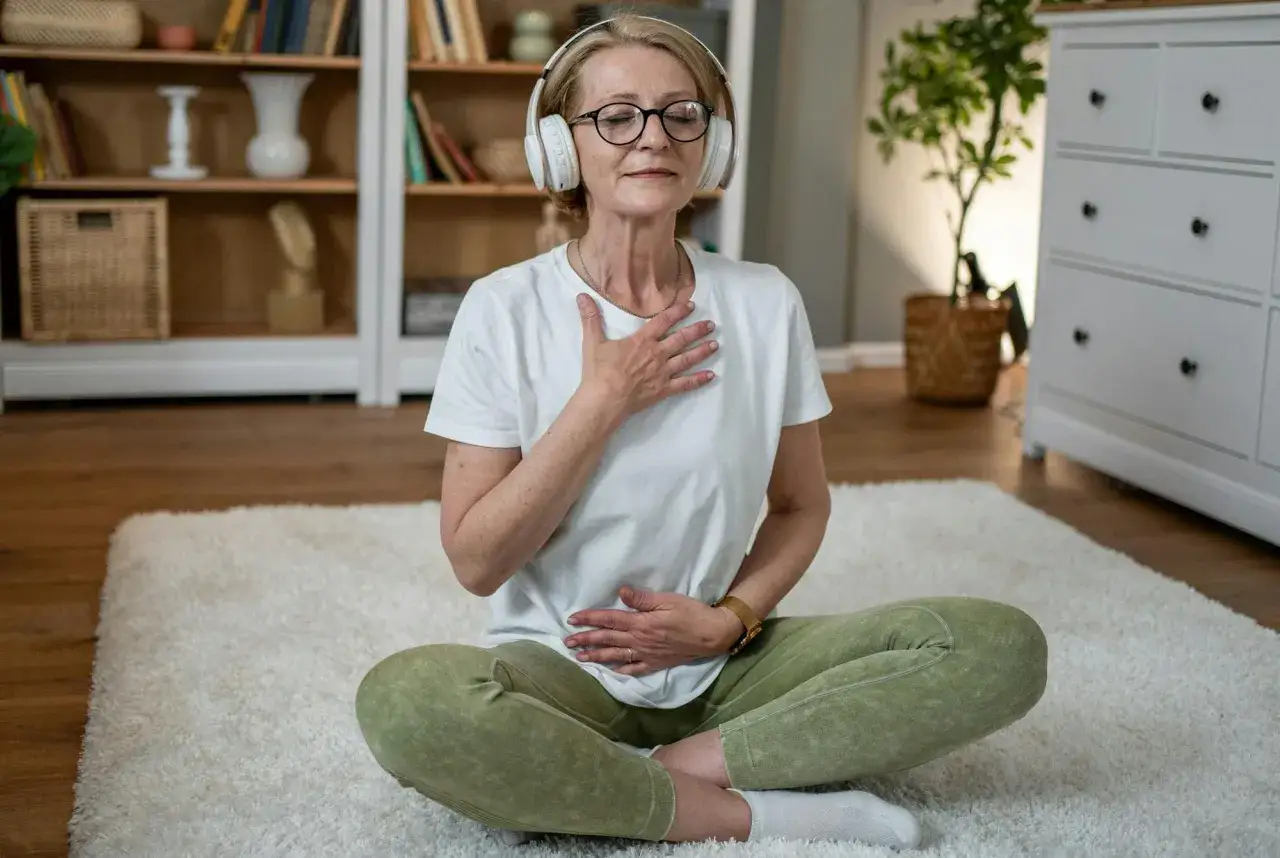 Kvinna med hörlurar mediterar och lägger handen på magen för att lugna en stressad mage.