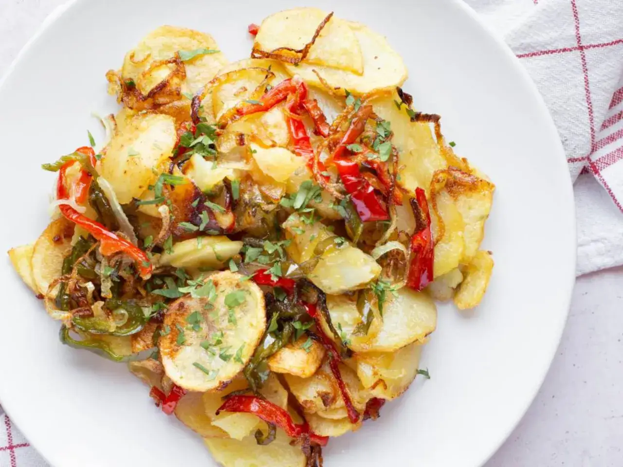 Patatas a lo pobre, un plato casero con patatas doradas, pimientos rojos y verdes, y cebolla, espolvoreado con perejil fresco.