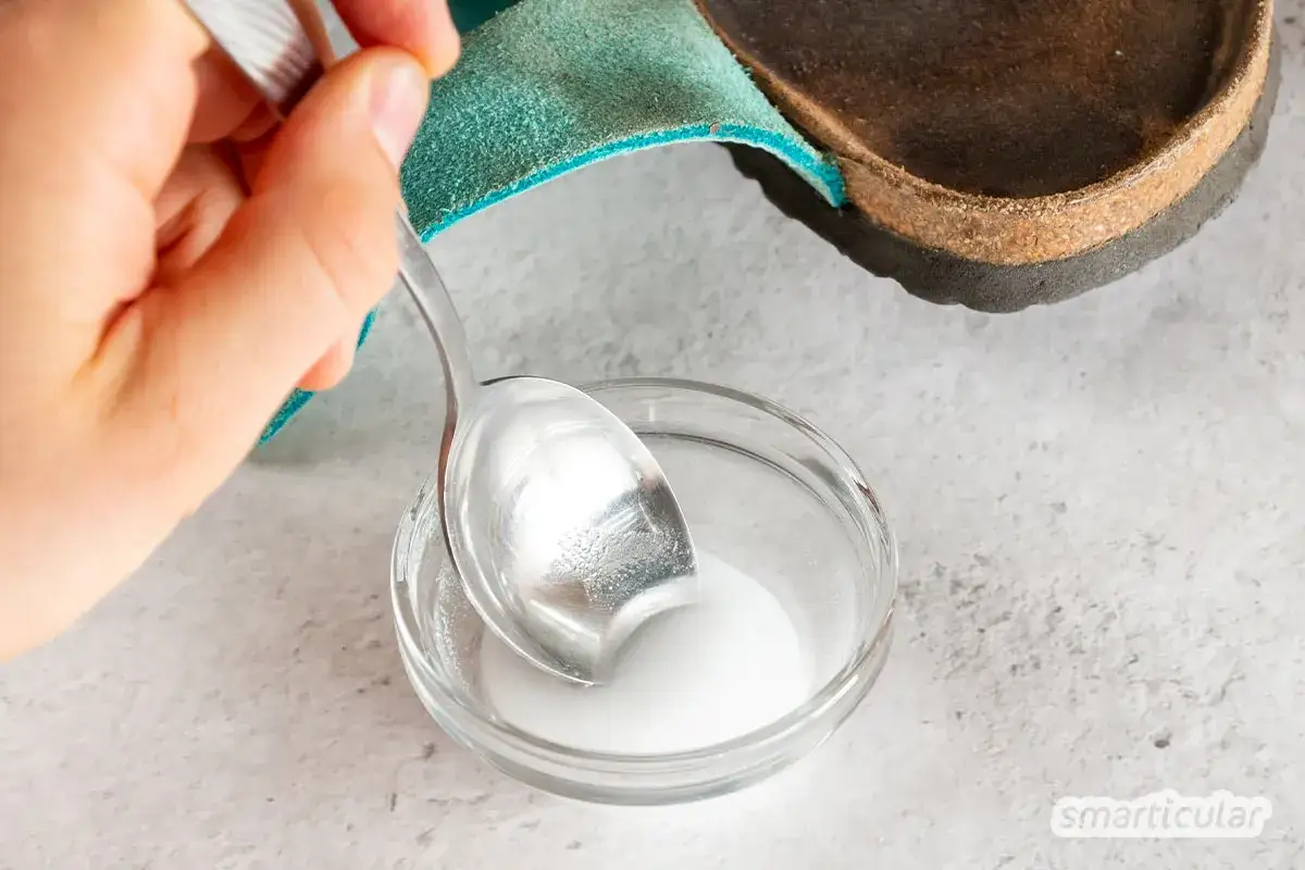 Hausmittel f&uuml;r sandalen innensohle reinigen: Eine Hand r&uuml;hrt mit einem L&ouml;ffel eine wei&szlig;e Paste in einer Sch&uuml;ssel an, um die Innensohle zu s&auml;ubern.