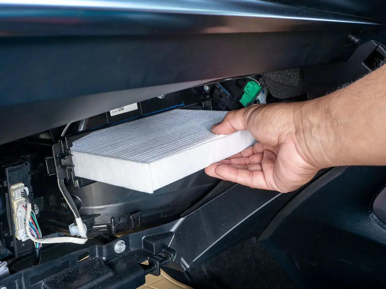 Mano insertando un filtro de aire nuevo en un coche. Preg&uacute;ntate cada cuanto se cambia el filtro de aire para mantener el aire limpio.