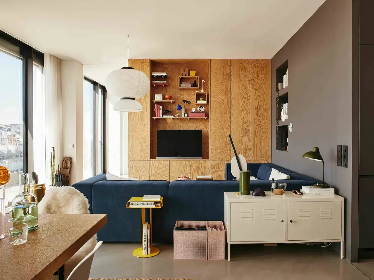 Un sal&oacute;n moderno con sof&aacute; azul, estanter&iacute;as de madera y l&aacute;mparas colgantes. Un espacio acogedor para **tini living**.