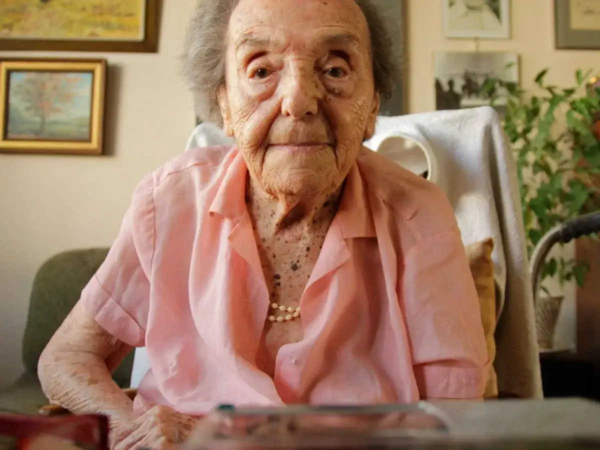 Alice Herz Sommer, eine ältere Dame in einem rosafarbenen Hemd, blickt nachdenklich in die Kamera.